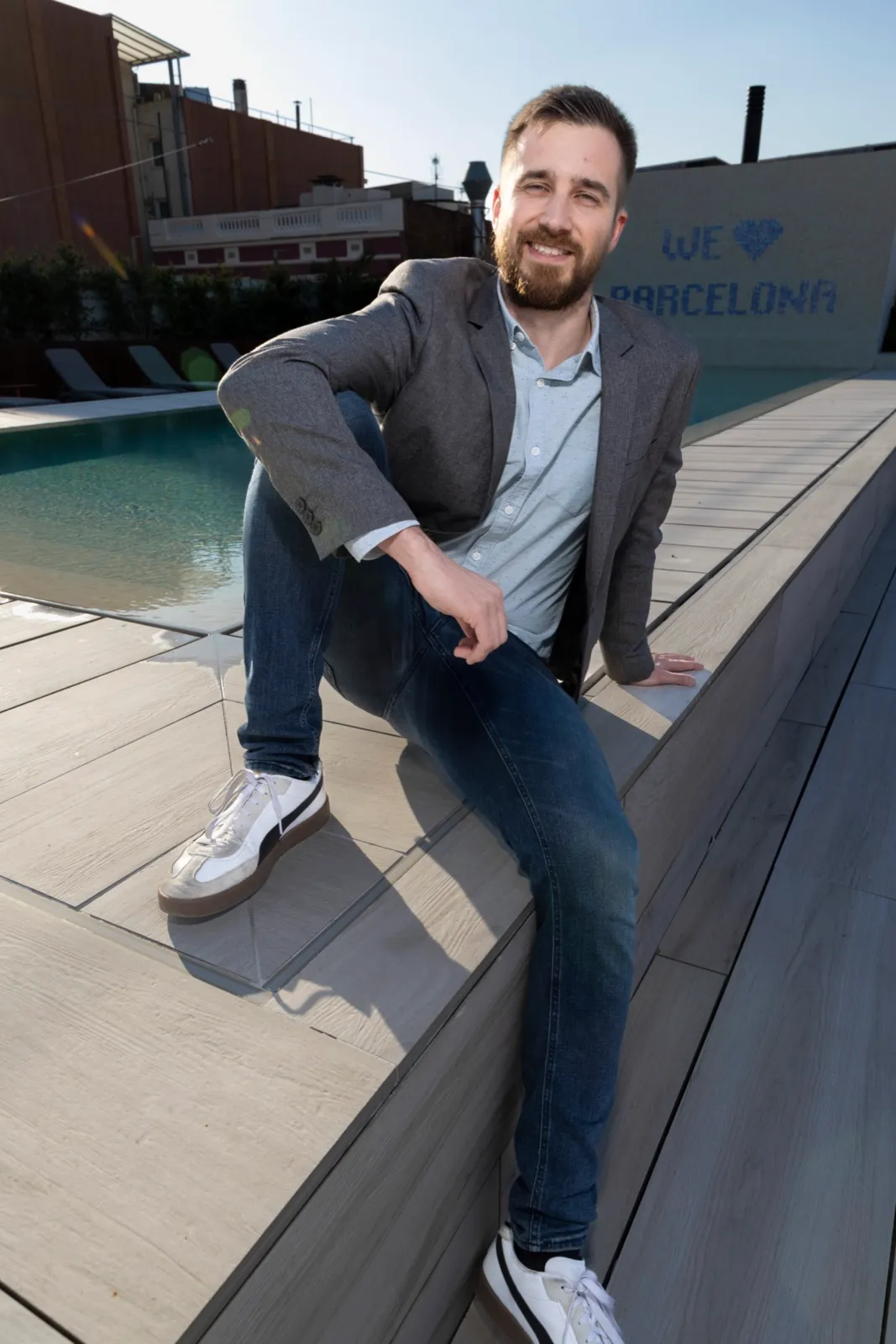Jakob assegut a la vora d’una piscina de terrat davant d’un mosaic que diu We love Barcelona, març del 2026.