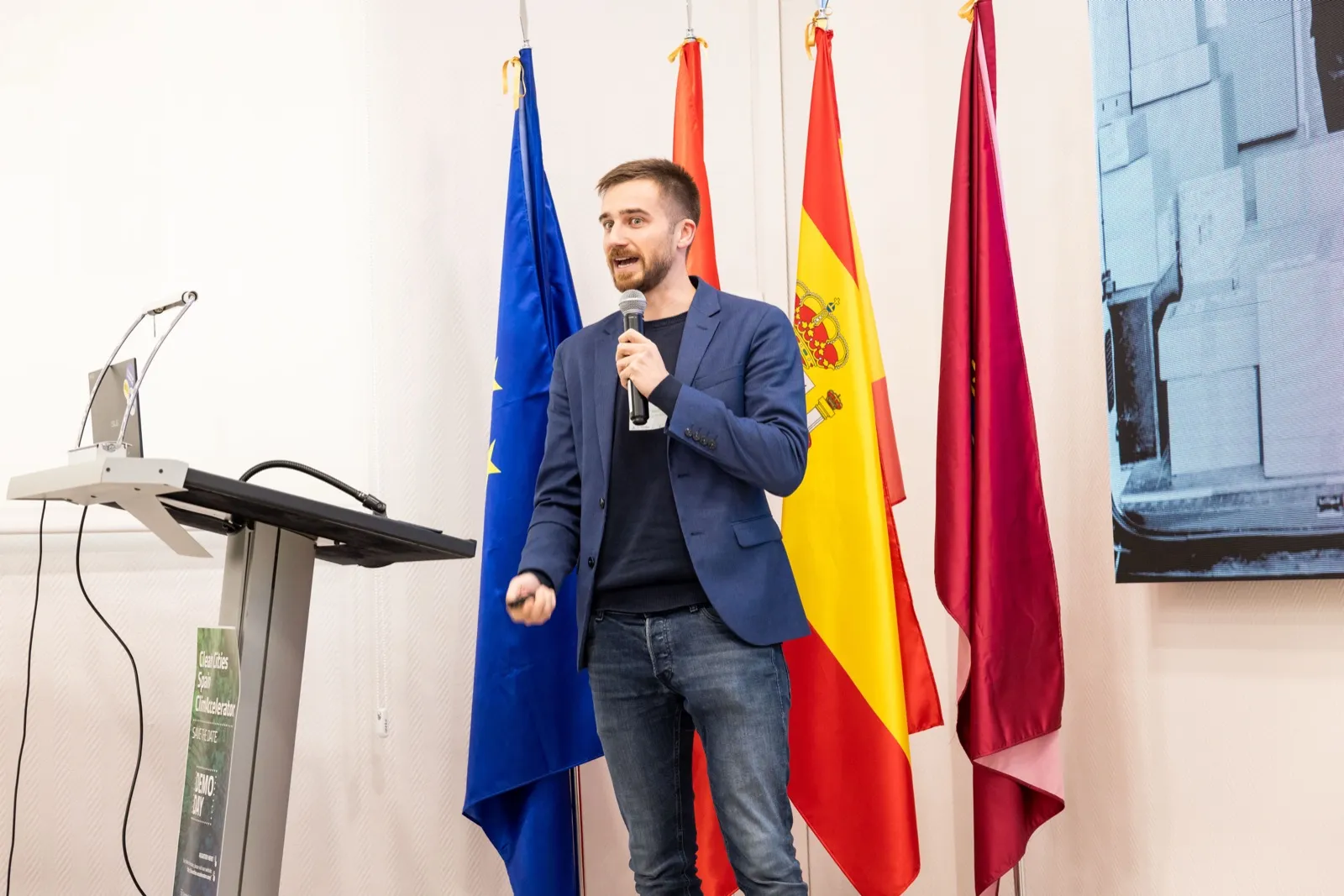 Jakob fent el pitch davant de banderes europees i espanyoles al demo day del Clean Cities ClimAccelerator a Madrid, octubre del 2025.